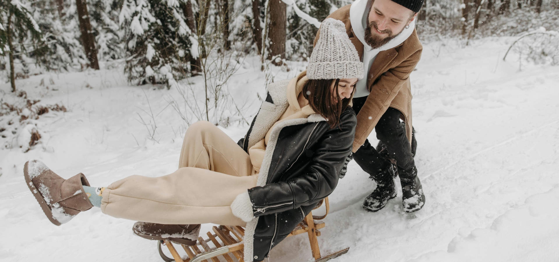 Koppel plezier makend met een slee tijdens een winterwandeling in een besneeuwd bos.