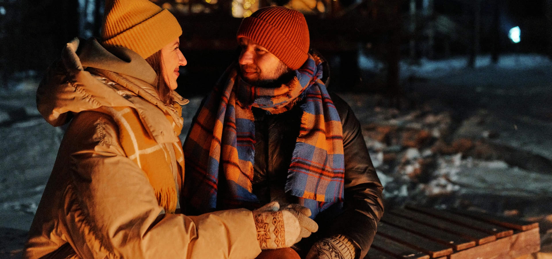 Twee mensen warm gekleed, zitten knus bij een kampvuur tijdens een winteravond.